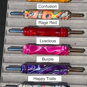May include: Six different colored crochet hooks with metal tips and gold accents. The hooks are labeled "Lemon", "Confusion", "Rage Red", "Luscious", "Burple", and "Happy Trails".