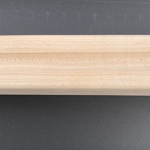 May include: A wooden fingerboard with a rounded shape and a groove in the center. The fingerboard is made of light wood and has a smooth surface.