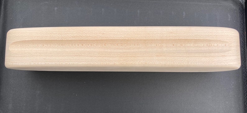 May include: A wooden fingerboard with a rounded shape and a groove in the center. The fingerboard is made of light wood and has a smooth surface.