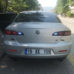 Puede incluir: Parte trasera de un sedán Alfa Romeo 159 plateado. El nombre del modelo y la matrícula son claramente visibles. Los faros traseros son rojos y blancos, y el coche tiene un sistema de escape doble.