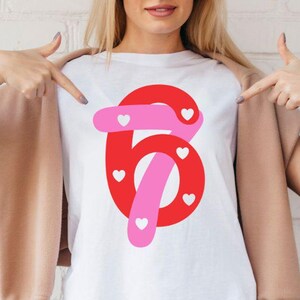 Könnte beinhalten: Weißes T-Shirt mit einem großen roten Zahl-Sechs-Design, akzentuiert mit rosa Elementen und kleinen weißen Herzen. Der Text "SVG & PNG Included!" ist links zu sehen, und eine sternförmige Grafik mit "Instant Digital Download" befindet sich rechts.