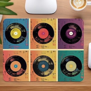 May include: A colourful mouse mat featuring six vintage vinyl records in a pop art style. The records are black with different coloured centres and are arranged in a grid pattern. The background is a mix of yellow, orange, blue, green, and purple.
