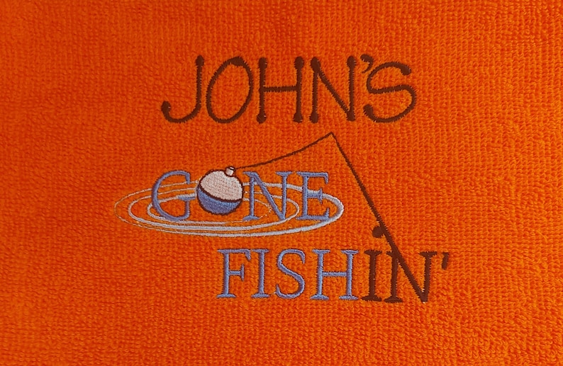 May include: An orange textured fabric featuring dark brown embroidered text that reads JOHN'S, followed by a light blue embroidered fishing bobber and line, with the light blue embroidered text GONE FISHIN' below it.