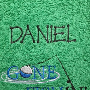May include: A bright green terry cloth towel featuring black embroidered text that reads DANIEL. Below the name is an embroidered fishing graphic with a blue and white bobber and the blue embroidered text GONE FISHIN'.