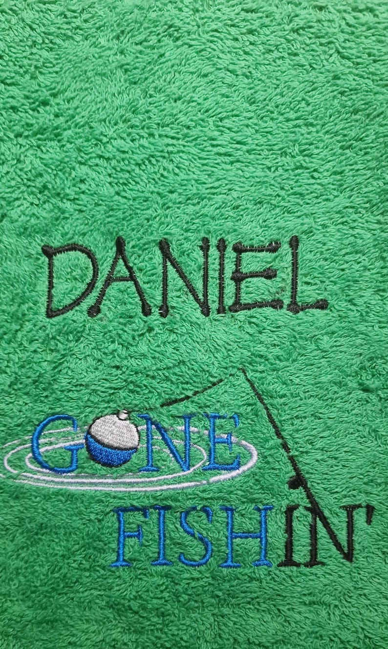 May include: A bright green terry cloth towel featuring black embroidered text that reads DANIEL. Below the name is an embroidered fishing graphic with a blue and white bobber and the blue embroidered text GONE FISHIN'.
