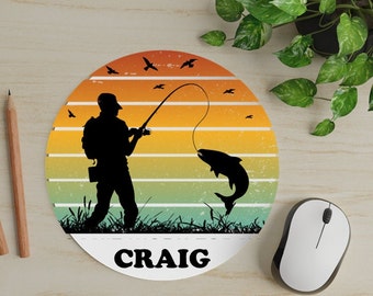 May include: A round mousepad with a retro sunset design featuring a silhouette of a person fishing. The mousepad has the name "CRAIG" printed in white at the bottom.