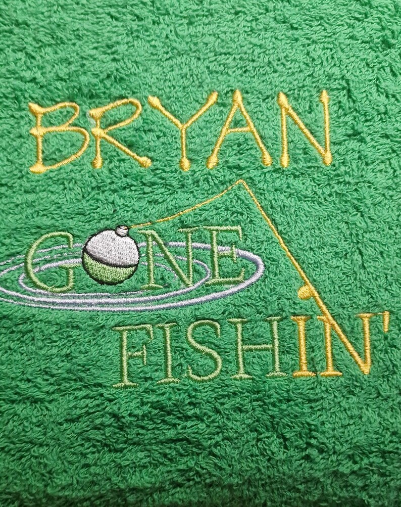 May include: A bright green towel featuring embroidered text that reads BRYAN GONE FISHIN'. The design includes a yellow fishing rod, a green and white bobber floating in water ripples, and yellow lettering for the name and the word FISHIN'.