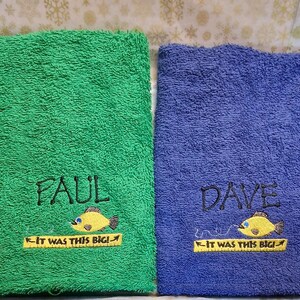 May include: Two rectangular terry cloth towels, one green and one blue. The green towel is embroidered with the name Paul, a yellow fish, and the text IT WAS THIS BIG! on a yellow ruler. The blue towel features the name Dave, a yellow fish, and the same text.