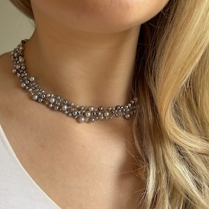 Puede incluir: Un collar gargantilla de cuentas plateadas y grises con un racimo de perlas.