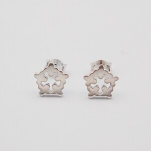May include: A pair of silver stud earrings with a delicate, intricate design featuring a cross shape within a circular frame.