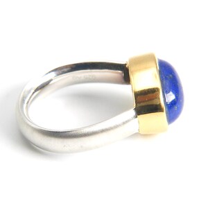 May include: A silver and gold ring with a blue lapis lazuli gemstone. The ring has a smooth, rounded band and a bezel setting for the stone.