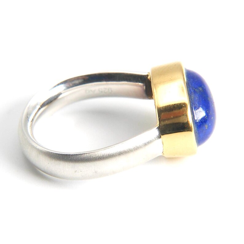 May include: A silver and gold ring with a blue lapis lazuli gemstone. The ring has a smooth, rounded band and a bezel setting for the stone.