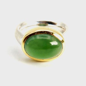 Può includere: Un anello d'argento con una montatura in oro e una pietra ovale verde.