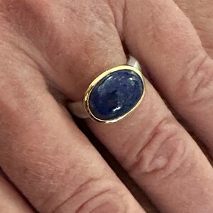 May include: A silver ring with a gold band and a blue oval gemstone.