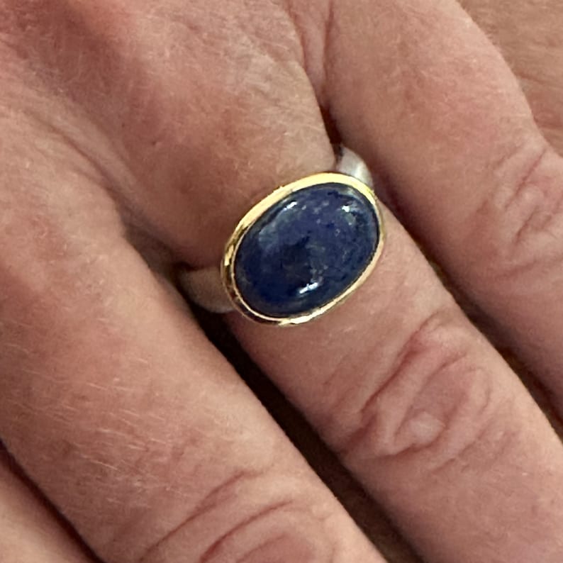 May include: A silver ring with a gold band and a blue oval gemstone.