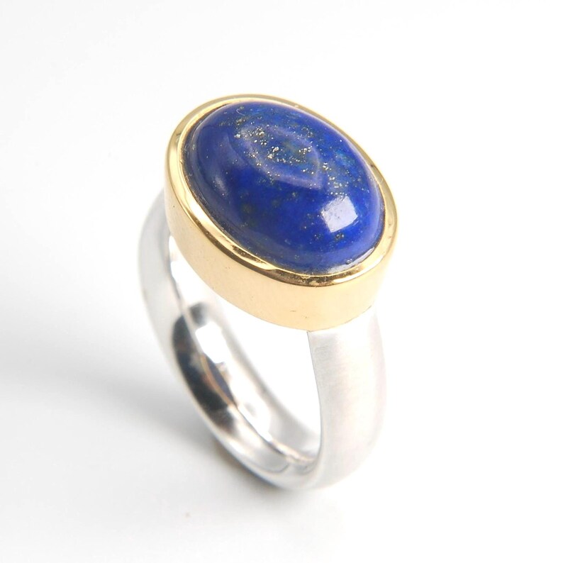 May include: A silver ring with a gold band set with a blue oval lapis lazuli gemstone.
