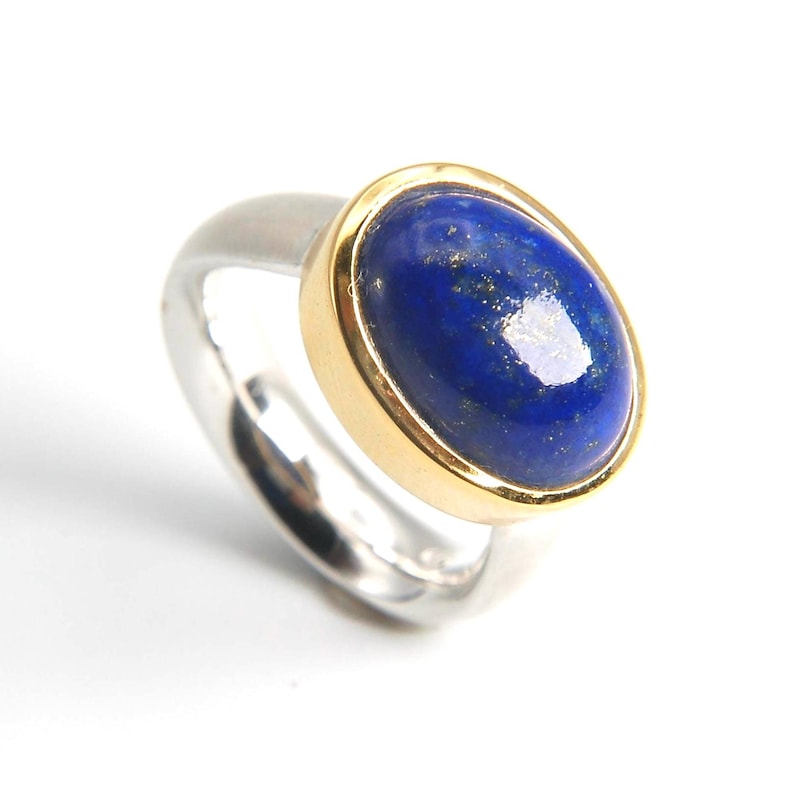 May include: A silver ring with a gold band set with a blue oval lapis lazuli gemstone.