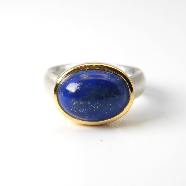 May include: A silver ring with a gold setting and a blue oval lapis lazuli gemstone.