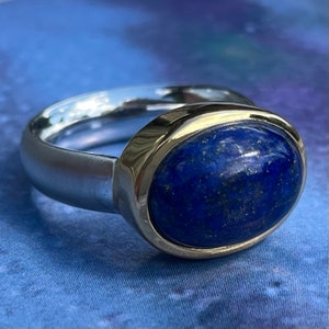 May include: A silver ring with a gold band and a large oval lapis lazuli gemstone.