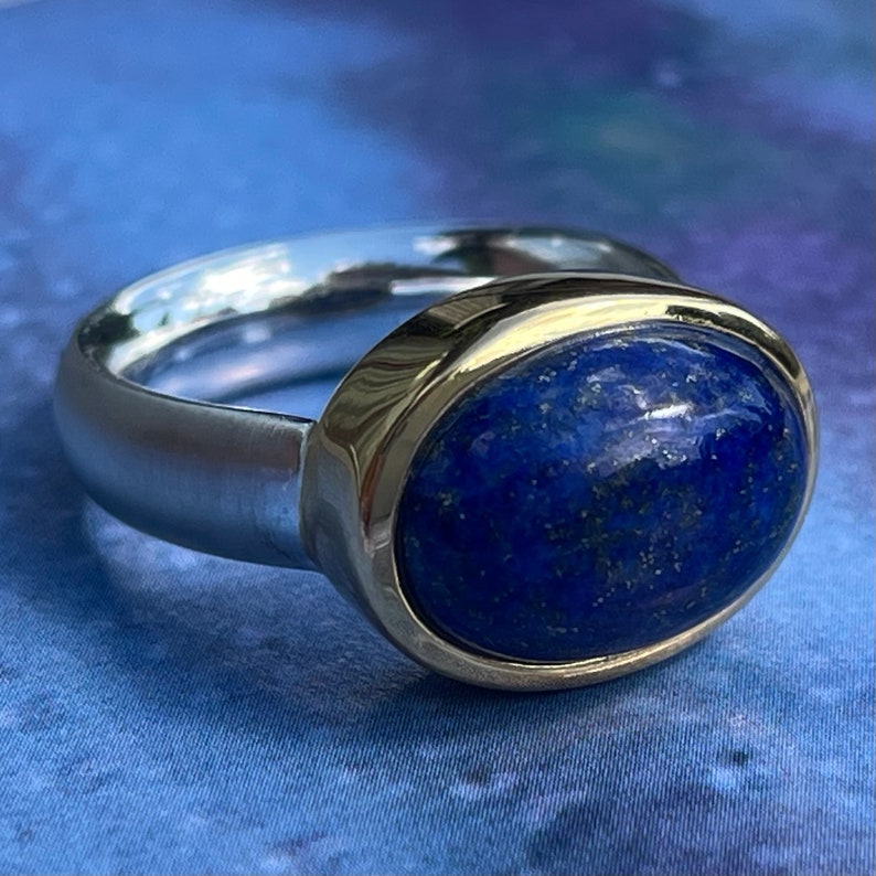 May include: A silver ring with a gold band and a large oval lapis lazuli gemstone.