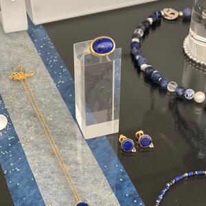 May include: A set of lapis lazuli jewelry featuring a ring, earrings, and a necklace. The ring and earrings have gold settings, while the necklace has a gold chain.