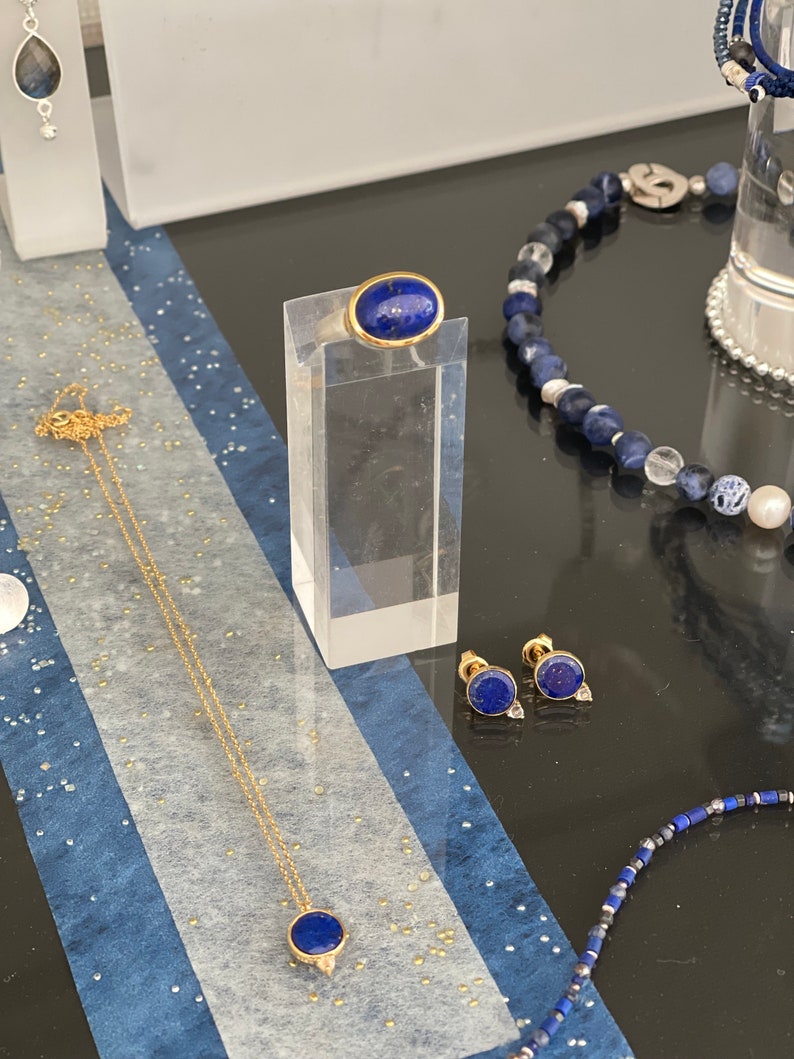 May include: A set of lapis lazuli jewelry featuring a ring, earrings, and a necklace. The ring and earrings have gold settings, while the necklace has a gold chain.
