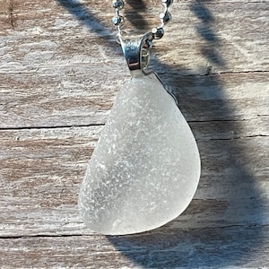 May include: A silver chain necklace with a white sea glass pendant. The pendant is a teardrop shape and has a frosted finish.