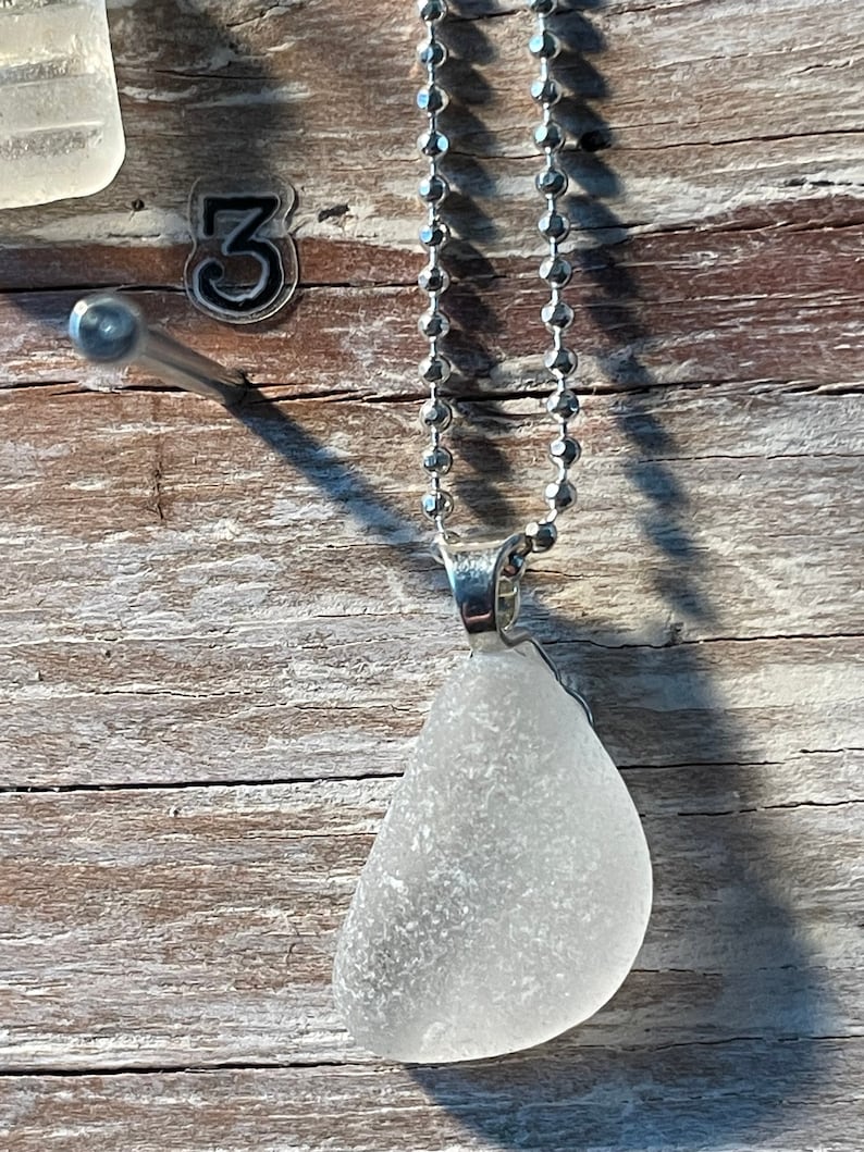 May include: A silver chain necklace with a white sea glass pendant. The pendant is a teardrop shape and has a frosted finish.