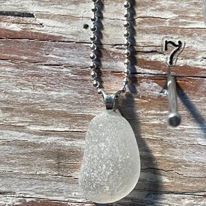 May include: A white sea glass pendant on a silver chain necklace. The pendant is a smooth, oval shape with a frosted finish.