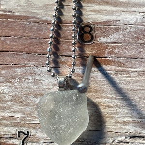 May include: A silver chain necklace with a clear, frosted glass pendant. The pendant is shaped like a heart and has a smooth, polished surface.