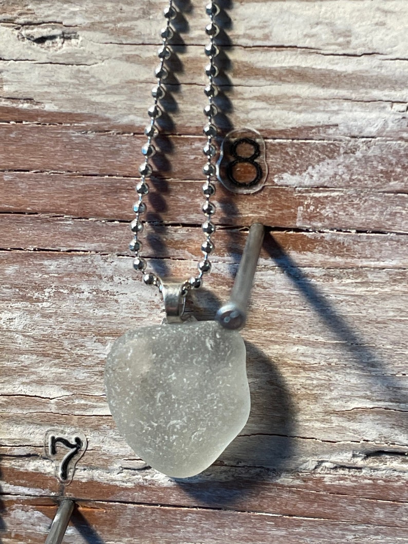 May include: A silver chain necklace with a clear, frosted glass pendant. The pendant is shaped like a heart and has a smooth, polished surface.