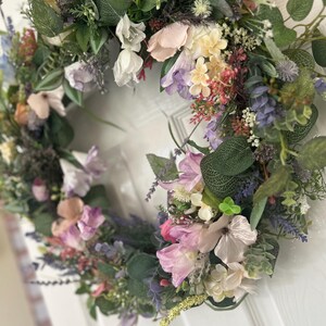 May include: A floral wreath with a variety of flowers in shades of pink, purple, white, and yellow, accented by green foliage. The wreath is likely for home decor.