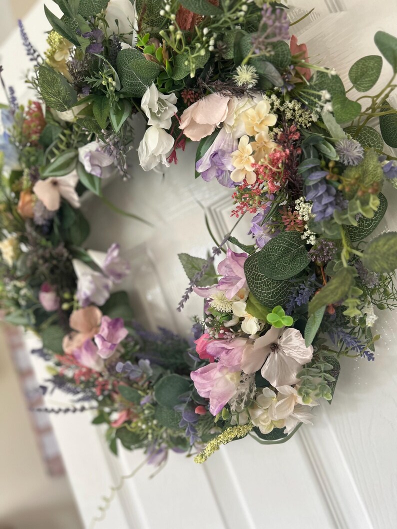 May include: A floral wreath with a variety of flowers in shades of pink, purple, white, and yellow, accented by green foliage. The wreath is likely for home decor.