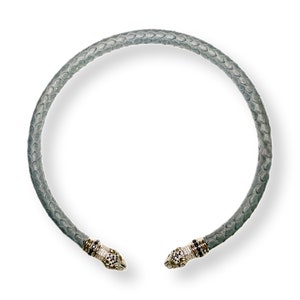 Könnte beinhalten: Graue Halskette mit Schlangenlederstruktur und dekorativen Enden. Die Enden der Halskette haben ein Schlangenkopf-Design mit schwarzen, weißen und goldenen Akzenten. Die Halskette wird auf weißem Hintergrund präsentiert.