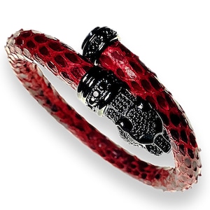 May include: A red and black snake-shaped bracelet. The bracelet is made of red snakeskin with black accents. The snake's head and tail are detailed with black gemstones. The bracelet is designed to wrap around the wrist.