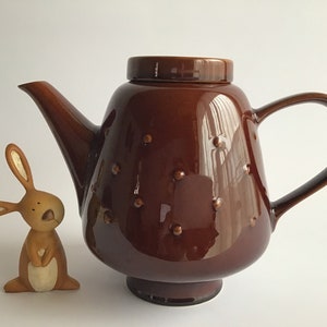 May include: A brown ceramic teapot with a textured surface and a rounded body. The teapot has a lid and a handle.