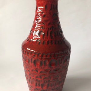 Peut inclure: Un vase en céramique rouge avec un bord noir et un motif texturé. Le vase a une base large et un col étroit.