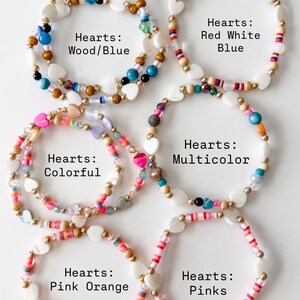 May include: Six circular beaded bracelets featuring white heart-shaped beads and various colored accents. The bracelets are labeled as Hearts: Wood/Blue, Red White Blue, Colorful, Multicolor, Pink Orange, and Pinks, showcasing diverse bead styles.