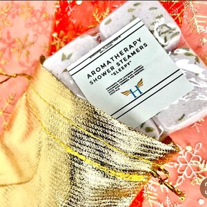 K&ouml;nnte beinhalten: Ein Set mit vier Aromatherapie-Duschdampfern in einer goldenen Tasche. Die Duschdampfer sind wei&szlig; und haben einen Lavendel-Duft. Das Etikett lautet "Aromatherapy Shower Steamers *Sleepy*"
