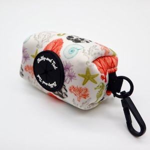 May include: White poop bag dispenser with a black clip and a black button with the text "Bailey and Ted" and "keep you happy" in white. The dispenser has a sea life pattern with coral, starfish, and seahorses.