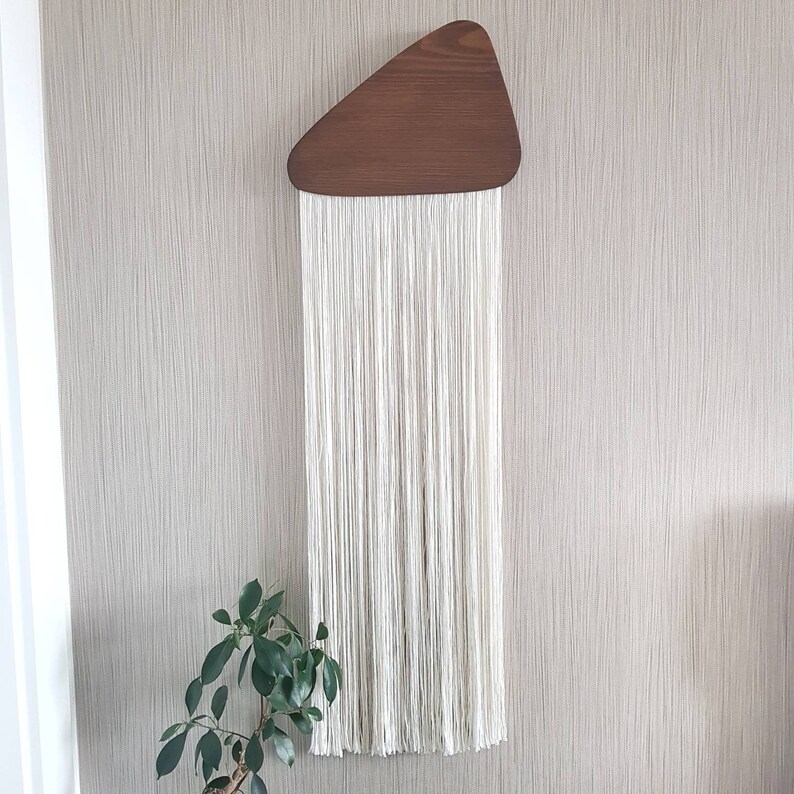 K&ouml;nnte beinhalten: Ein wei&szlig;er Makramee-Wandbehang mit einer dreieckigen Holzform oben.