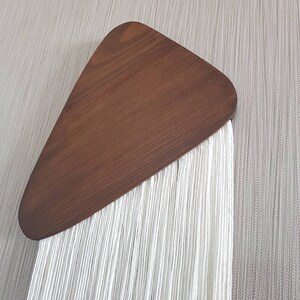 K&ouml;nnte beinhalten: Ein wei&szlig;er Makramee-Wandbehang mit einem braunen Holzdreieck oben.