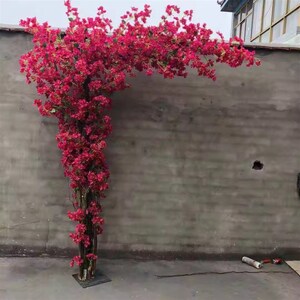 May include: A large artificial flower arrangement with pink blossoms cascading down a metal frame. The flowers are arranged in a way that resembles a vine or a bush. The frame is attached to a base, and the arrangement is placed against a gray wall.