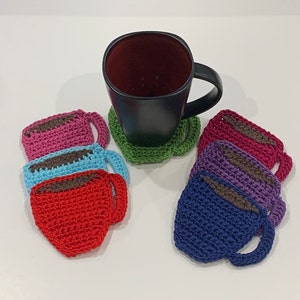 May include: Set of six crocheted coffee cup coasters in various colors, including red, blue, purple, pink, and green. Each coaster features a crocheted coffee cup design with a brown crocheted handle.