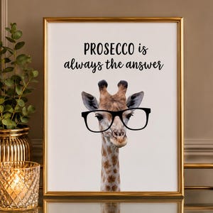 May include: A framed wall art print featuring a realistic giraffe wearing large black-rimmed glasses. The text above the giraffe reads, "PROSECCO is always the answer" in a combination of bold sans-serif and elegant script black lettering.