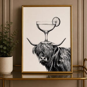 May include: A black and white framed art print featuring a shaggy Highland cow with a stemmed cocktail glass balanced between its horns. The glass contains a liquid and a circular citrus slice garnish, rendered in a detailed sketch style.