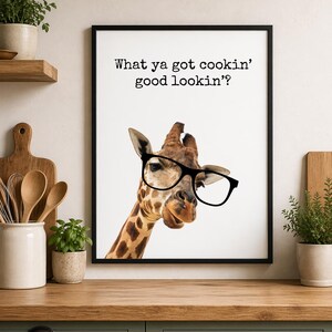 May include: A framed print featuring a giraffe wearing black glasses. The giraffe has a brown and tan spotted pattern. The print has the text "What ya got cookin' good lookin'?" in black font on a white background.