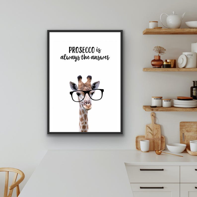 May include: A framed wall art print featuring a giraffe wearing black-rimmed glasses. The text above the giraffe reads, "PROSECCO is always the answer" in a black sans-serif font. The background of the print is white, and the frame is black.