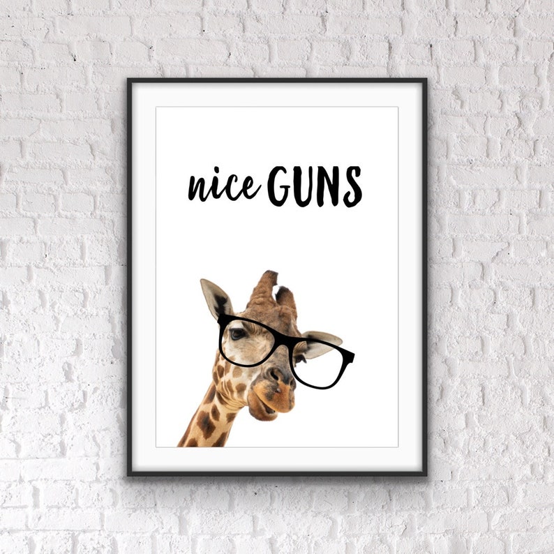 May include: Framed art print featuring a giraffe wearing black glasses. The text "nice GUNS" is printed above the giraffe's head in a black, handwritten-style font. The giraffe has a brown and tan spotted pattern.