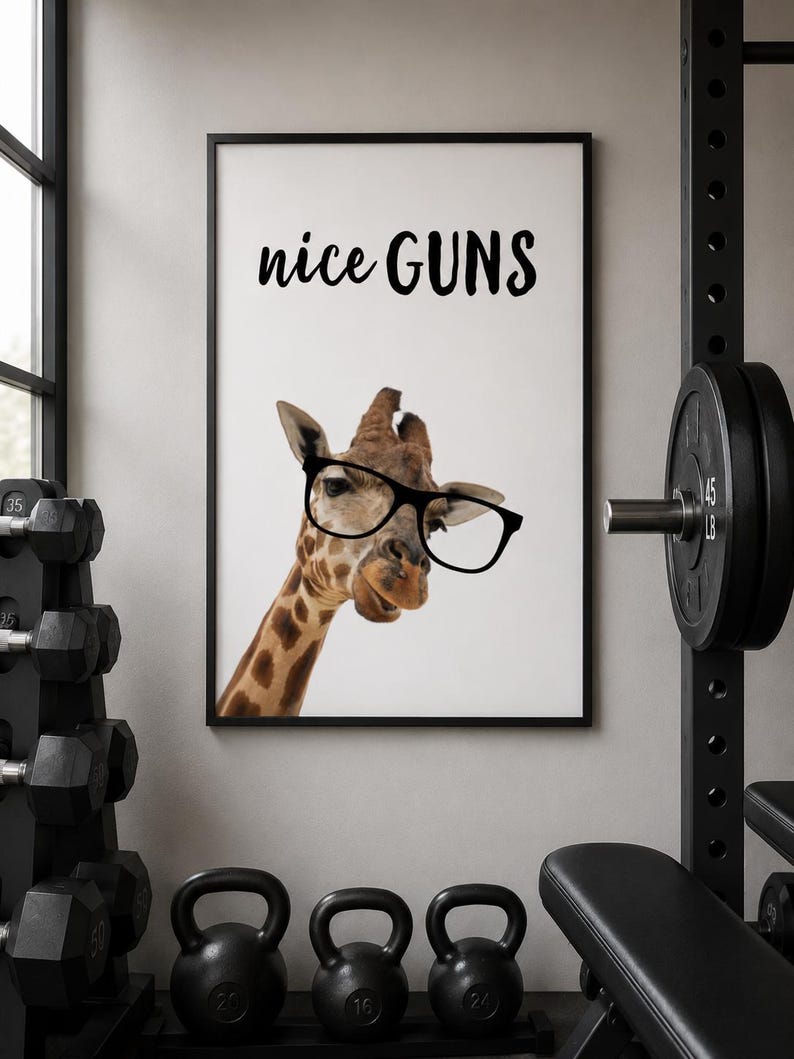 May include: A framed print featuring a giraffe wearing glasses with the text "nice GUNS" in black. The image is set in a gym with weights and a bench in the background. The giraffe has a brown and tan pattern.